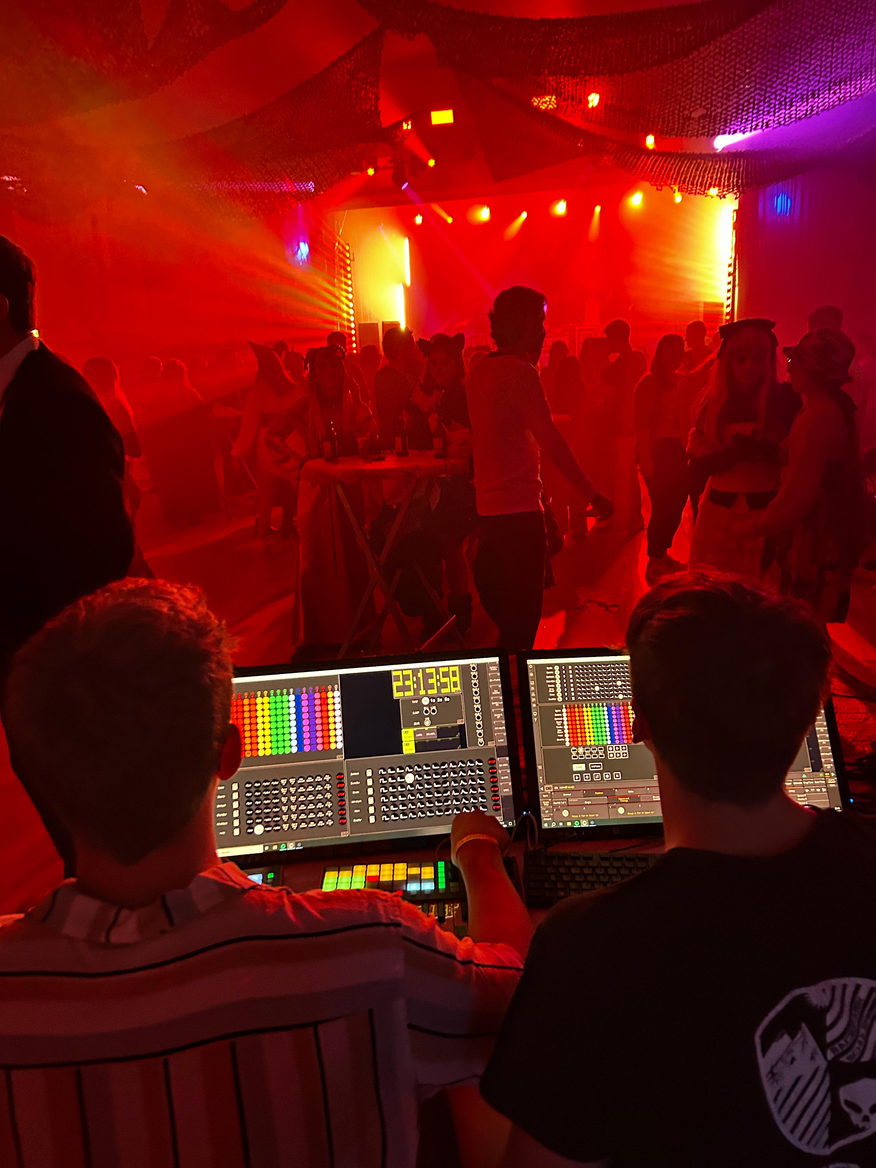 Djs an Pult vor einer farbig beleuchteten Tanzfläche mit Menschen